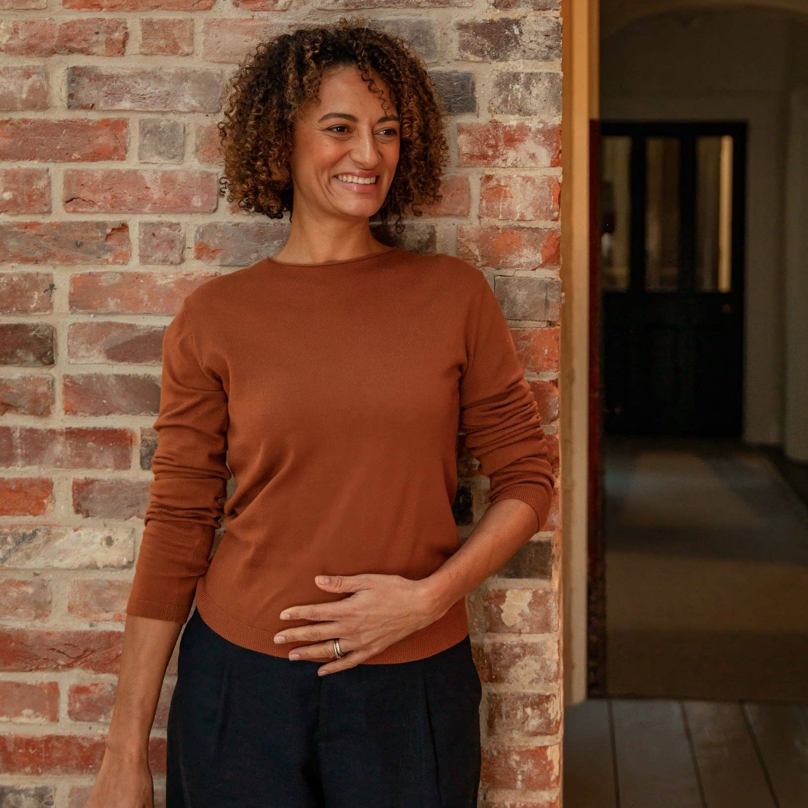 Woman in a brown sweater standing against a brick wall