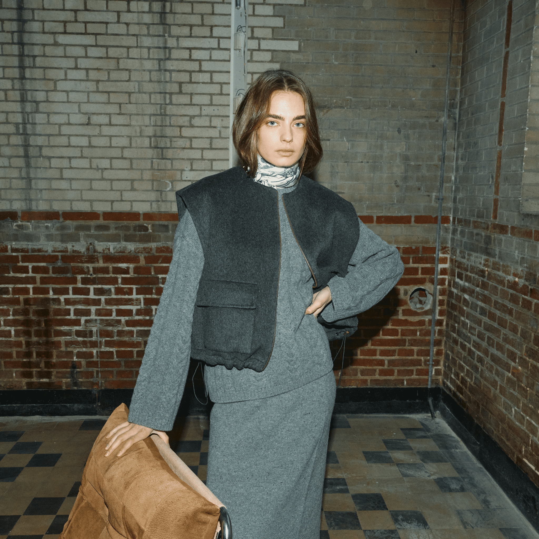 Person wearing a grey outfit standing in a brick-walled room.
