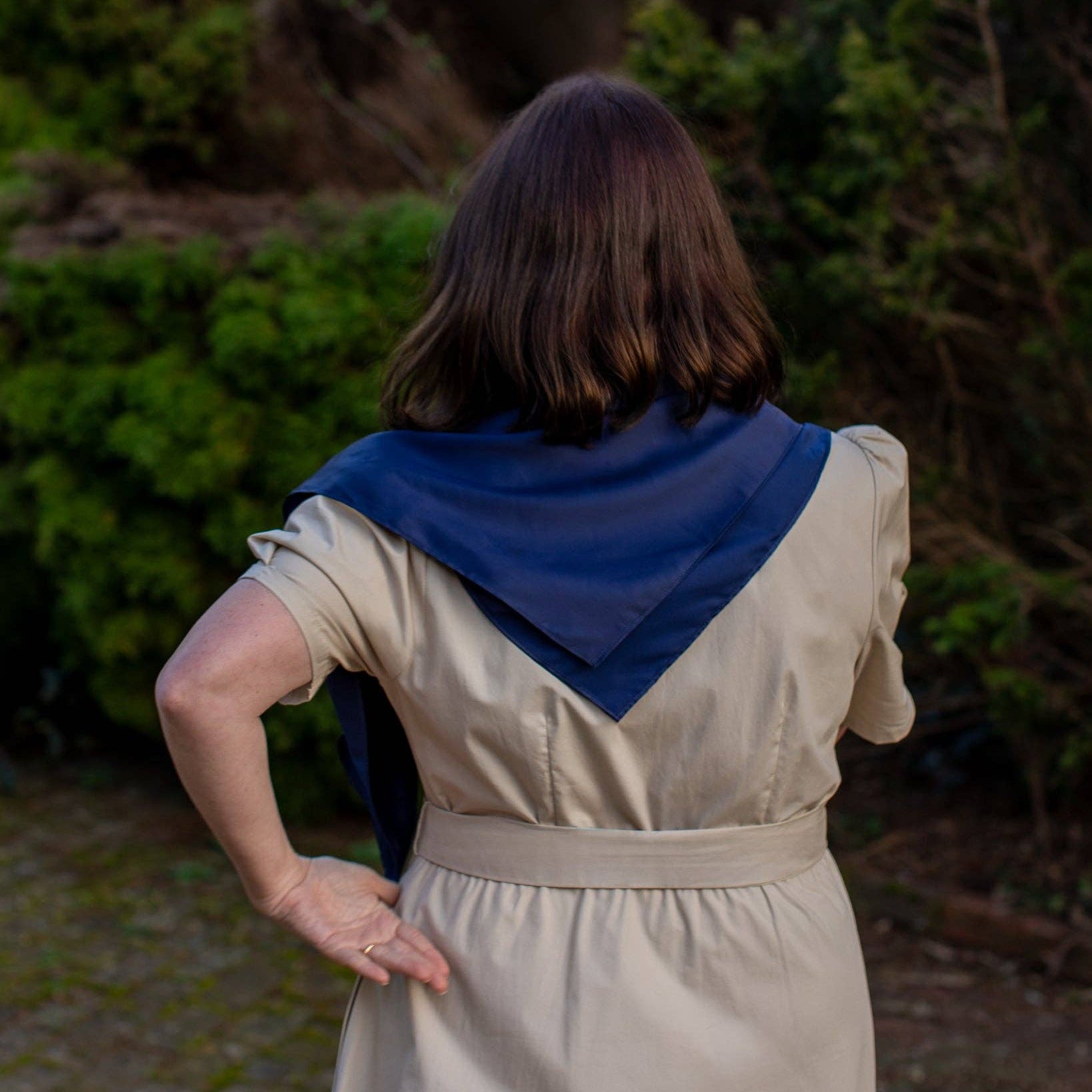 Woman wearing a beige dress with a blue scarf in an outdoor setting