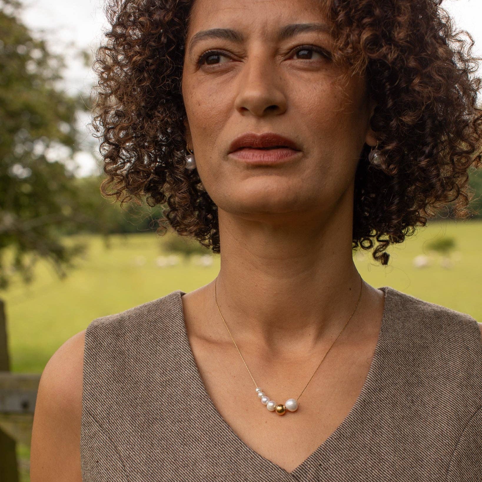Woman wearing a brown sleeveless top with a necklace in an outdoor setting