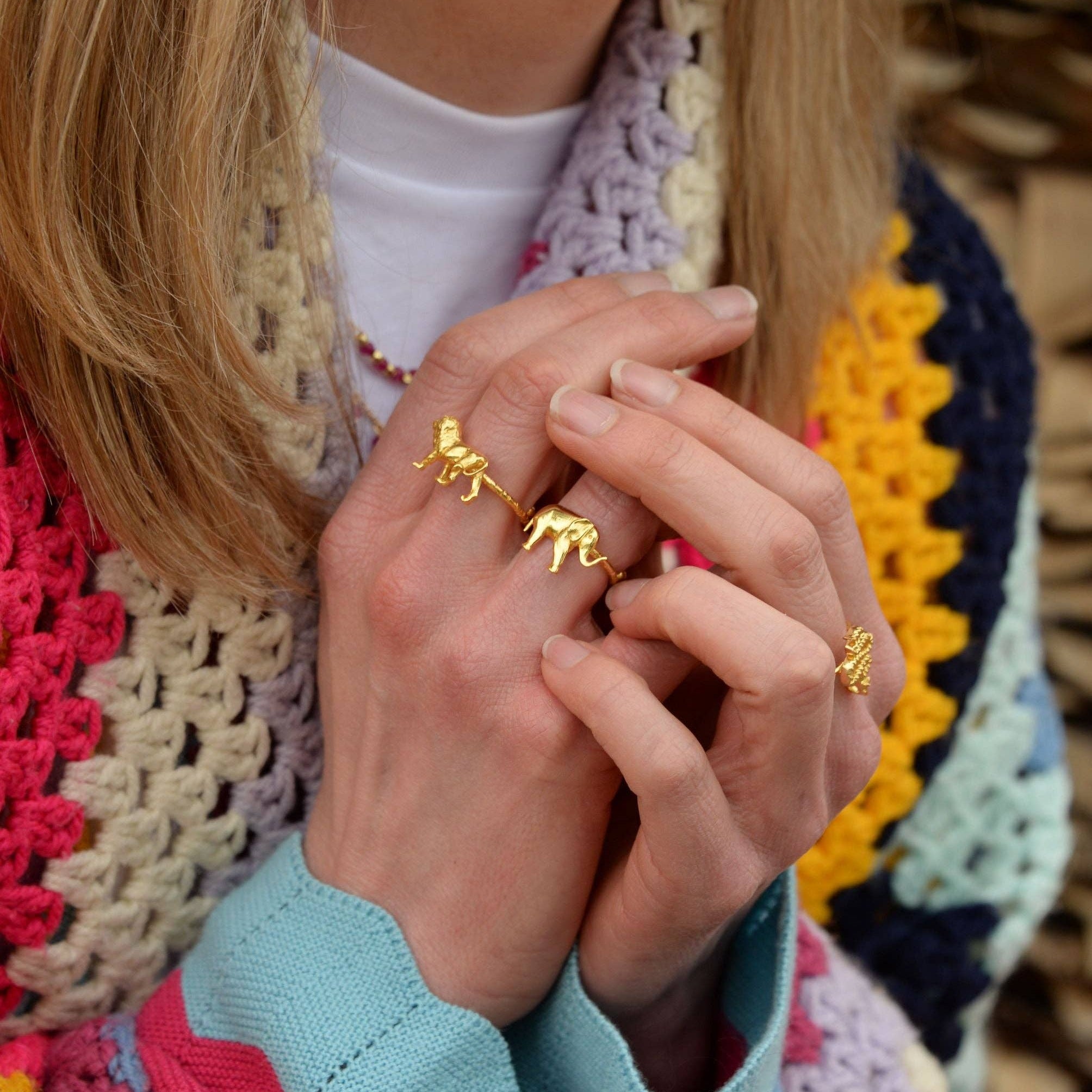 Close-up of hands wearing gold rings with a colorful textured garment in the background
