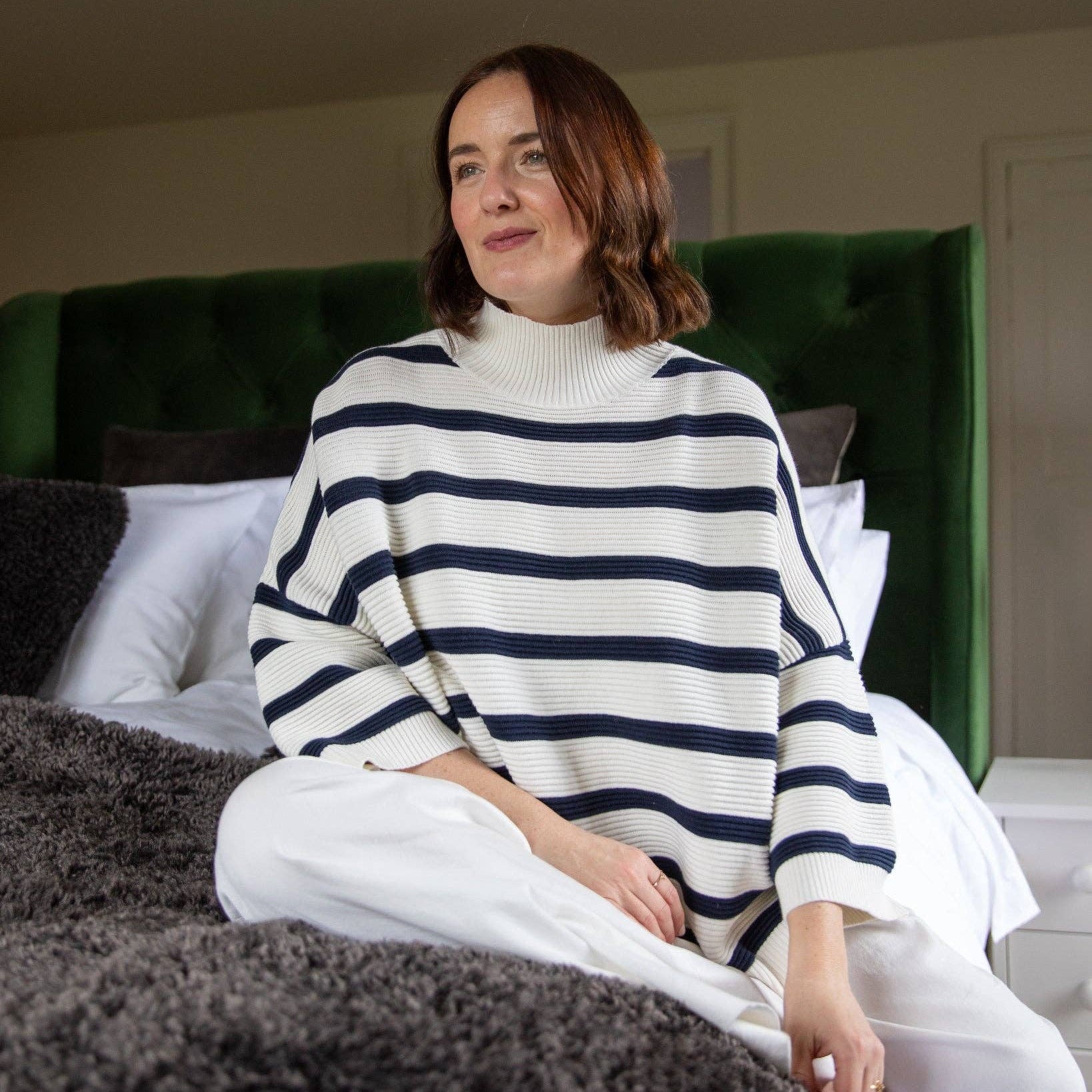 Woman wearing a striped sweater sitting on a bed with a green headboard.