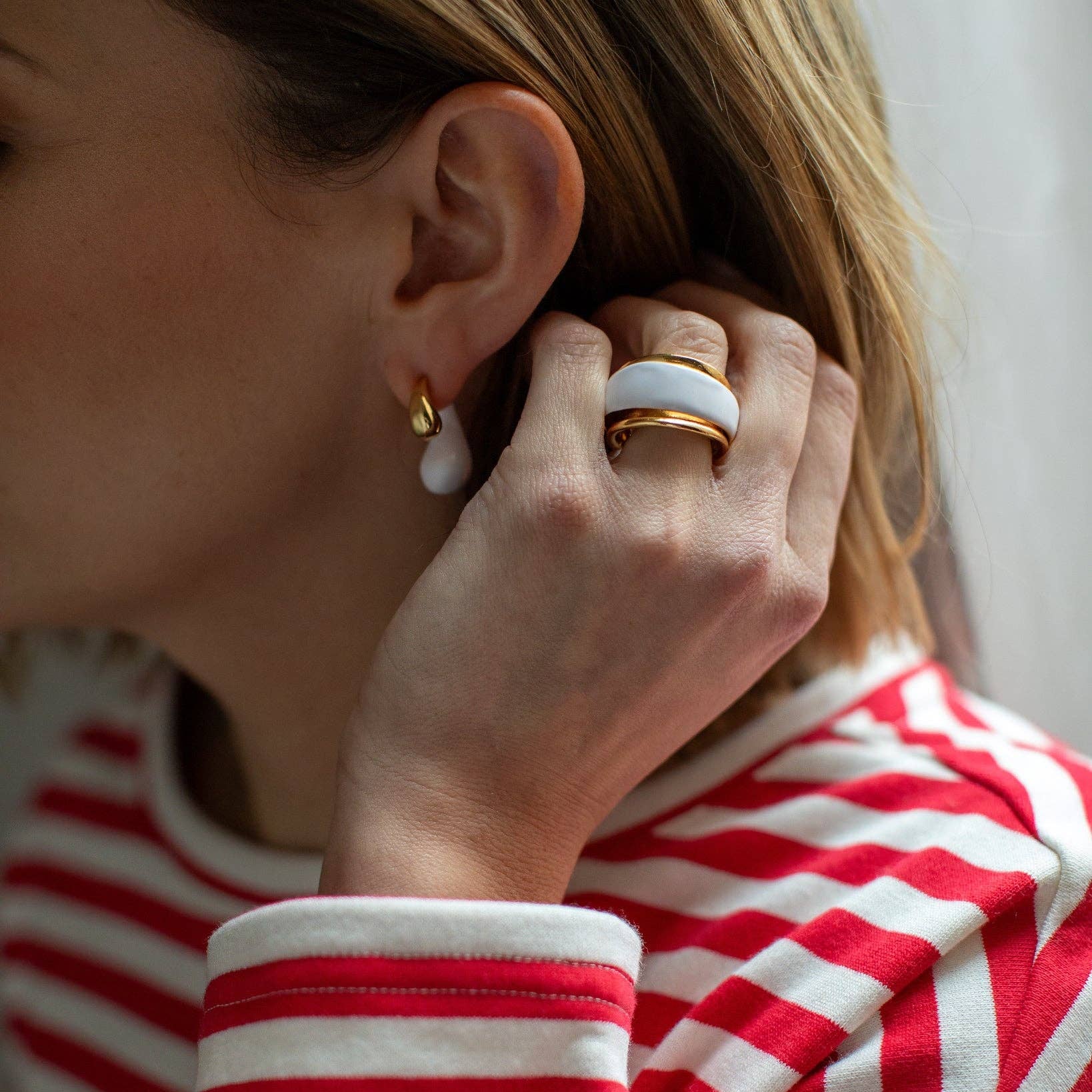 Person wearing a red and white striped shirt with a close-up of an earring and ring.