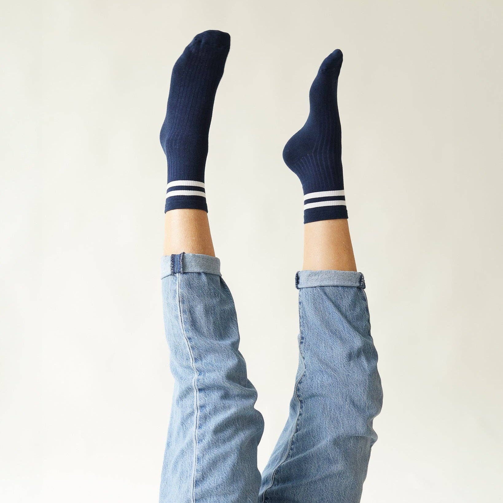 Person wearing navy socks with white stripes and light blue jeans against a plain background
