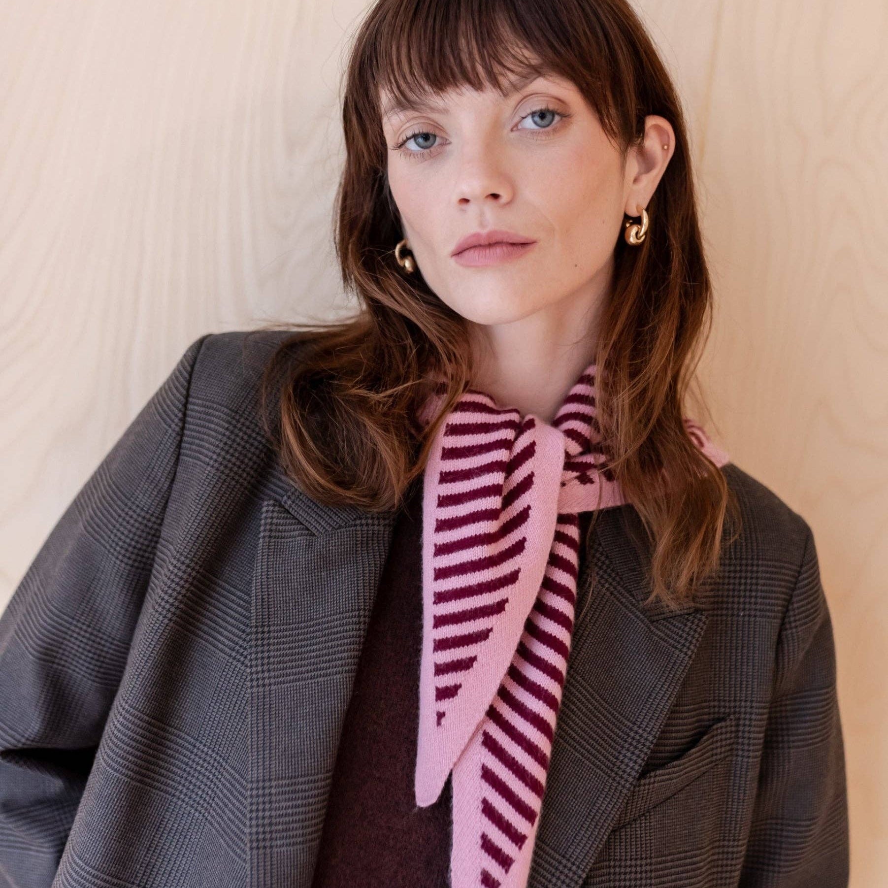 Woman wearing a gray coat and pink striped scarf against a beige background