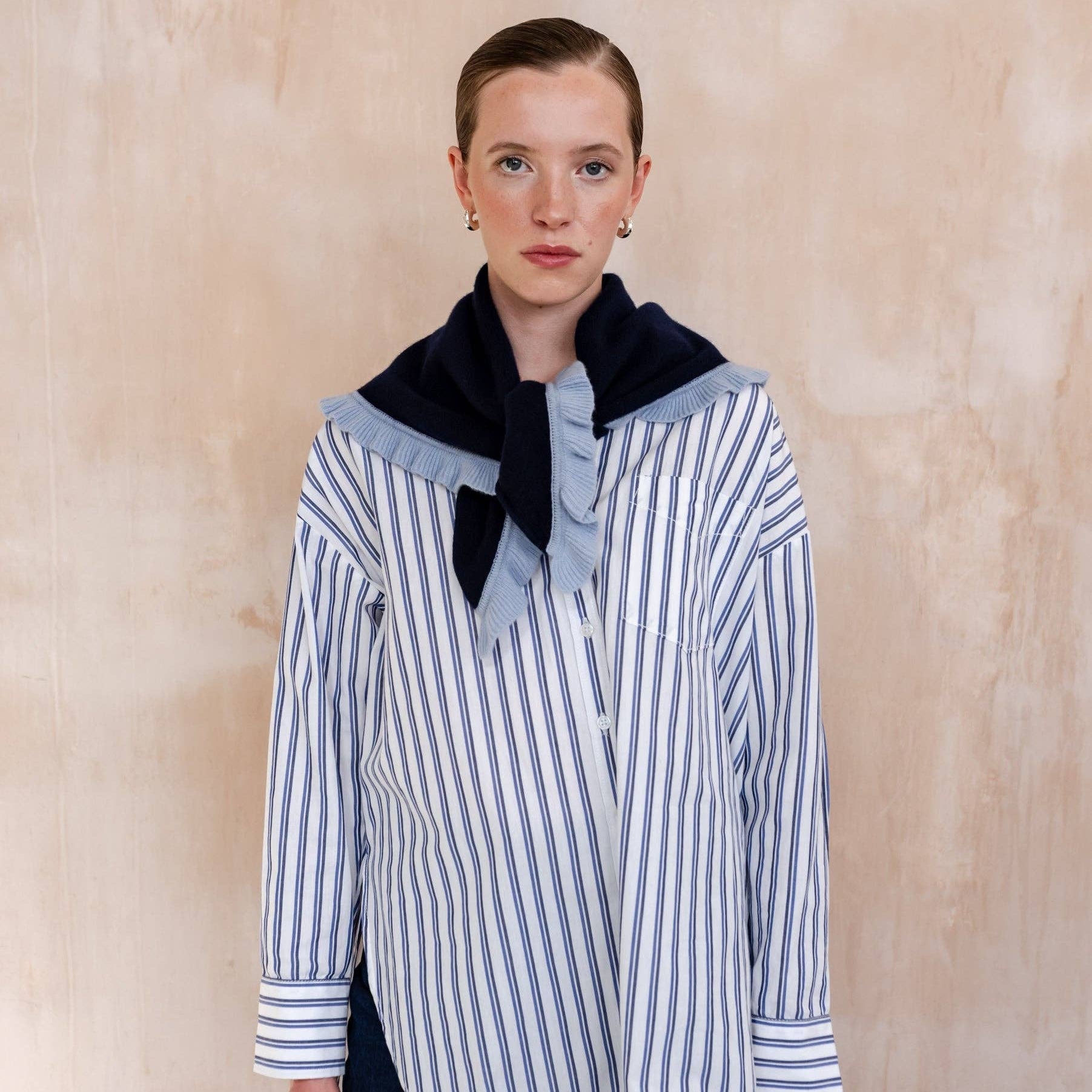 Person wearing a striped shirt with a navy ruffle triangle scarf