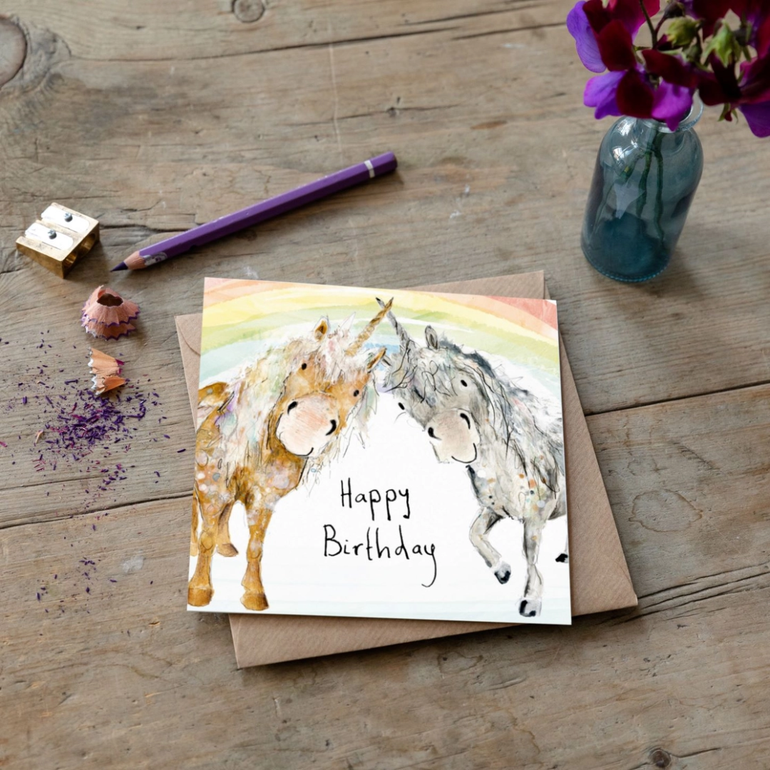 A desk scene with a card featuring two unicorns touching horns with the words Happy Birthday