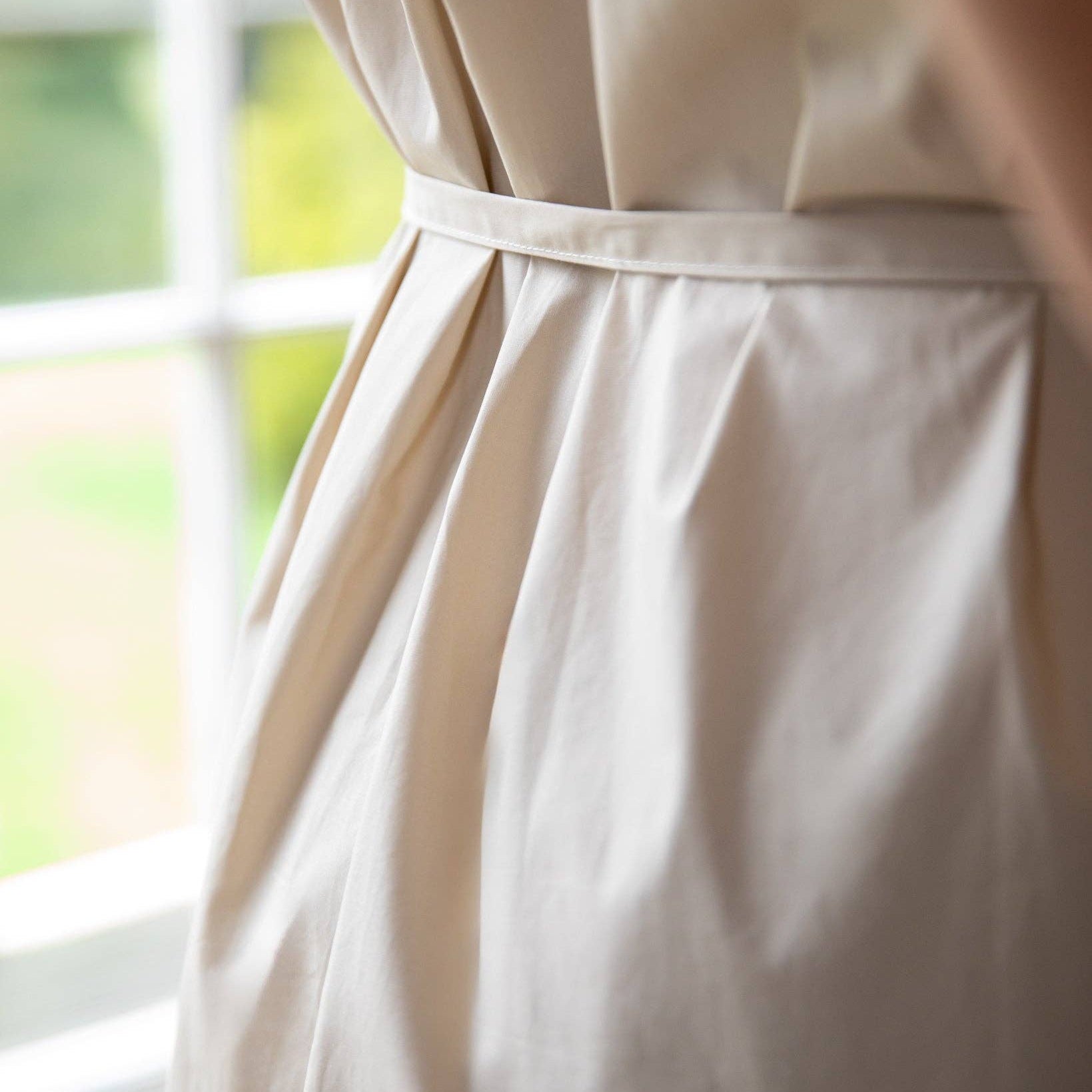 Close-up of a beige dress with a belt in front of a window
