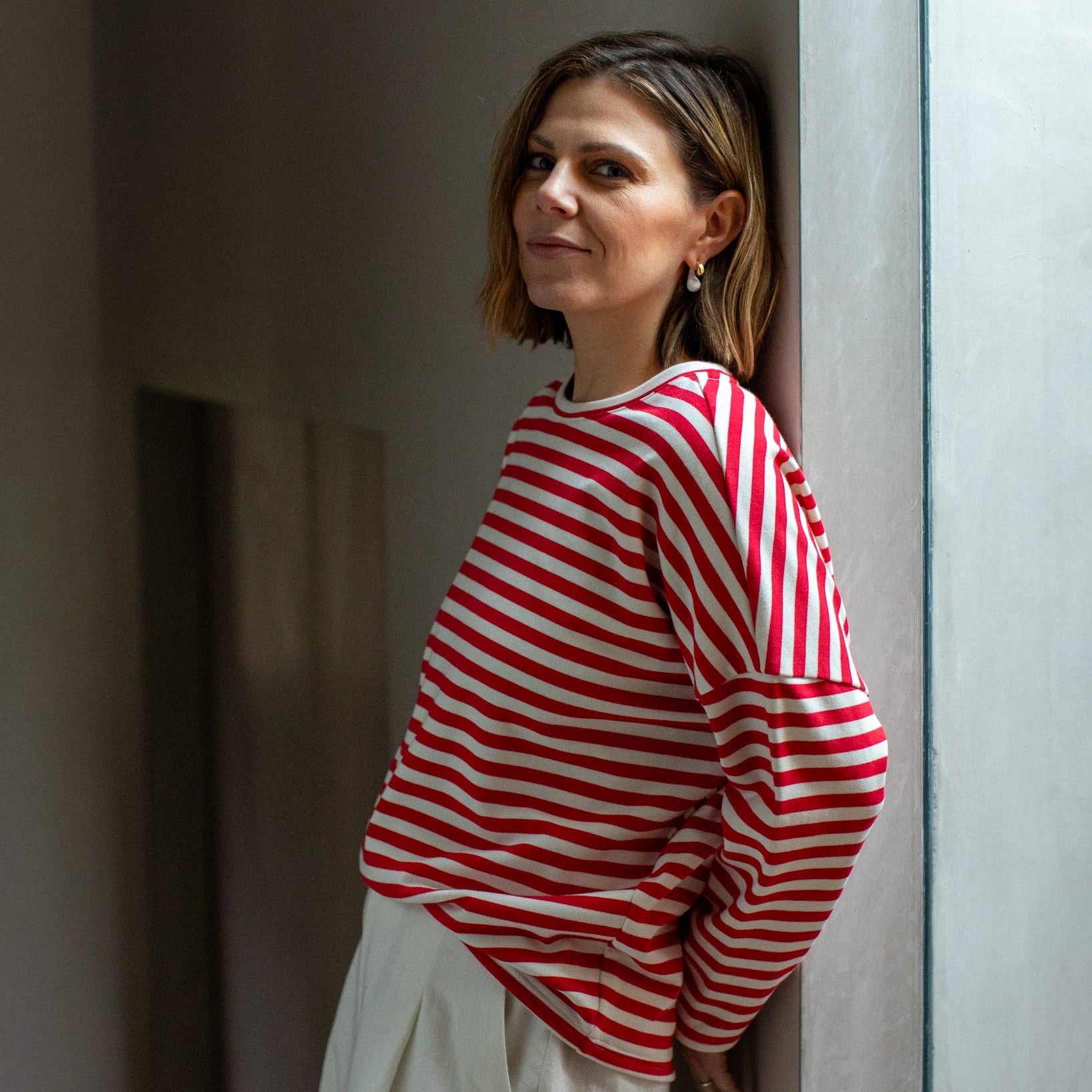 Woman wearing a red and white striped sweater standing against a neutral wall.