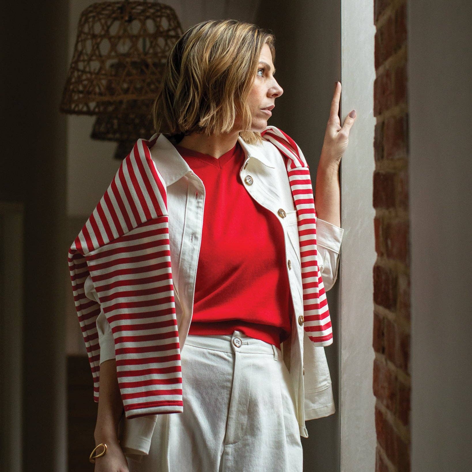 Woman wearing a red and white striped jacket over a red shirt in a room with brick walls.