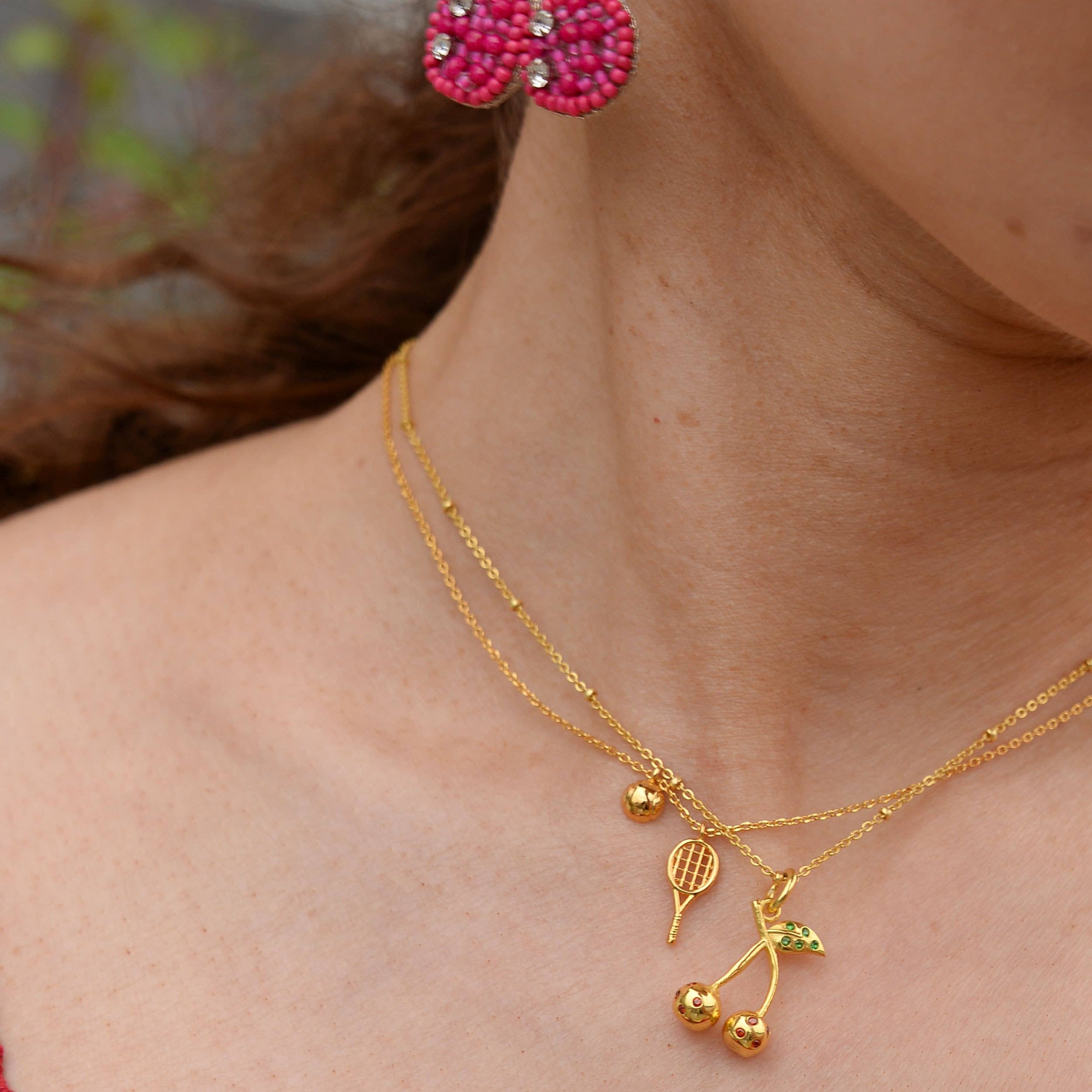 Close-up of a person wearing gold earrings and necklace with cherry design.