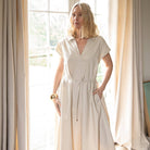 Woman wearing a beige dress standing in a bright room with large windows and curtains.