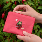 Hand holding a pink embroidered wallet by My Doris with flowers against a green leafy background