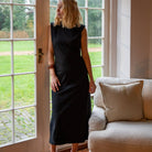 Woman in a black dress standing in a room with a couch and large window.