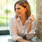 Woman in a white shirt sitting at a table with a blurred outdoor background