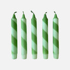 Five green and white striped candles on a light gray background
