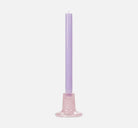 Purple candle on a pink ceramic holder against a white background
