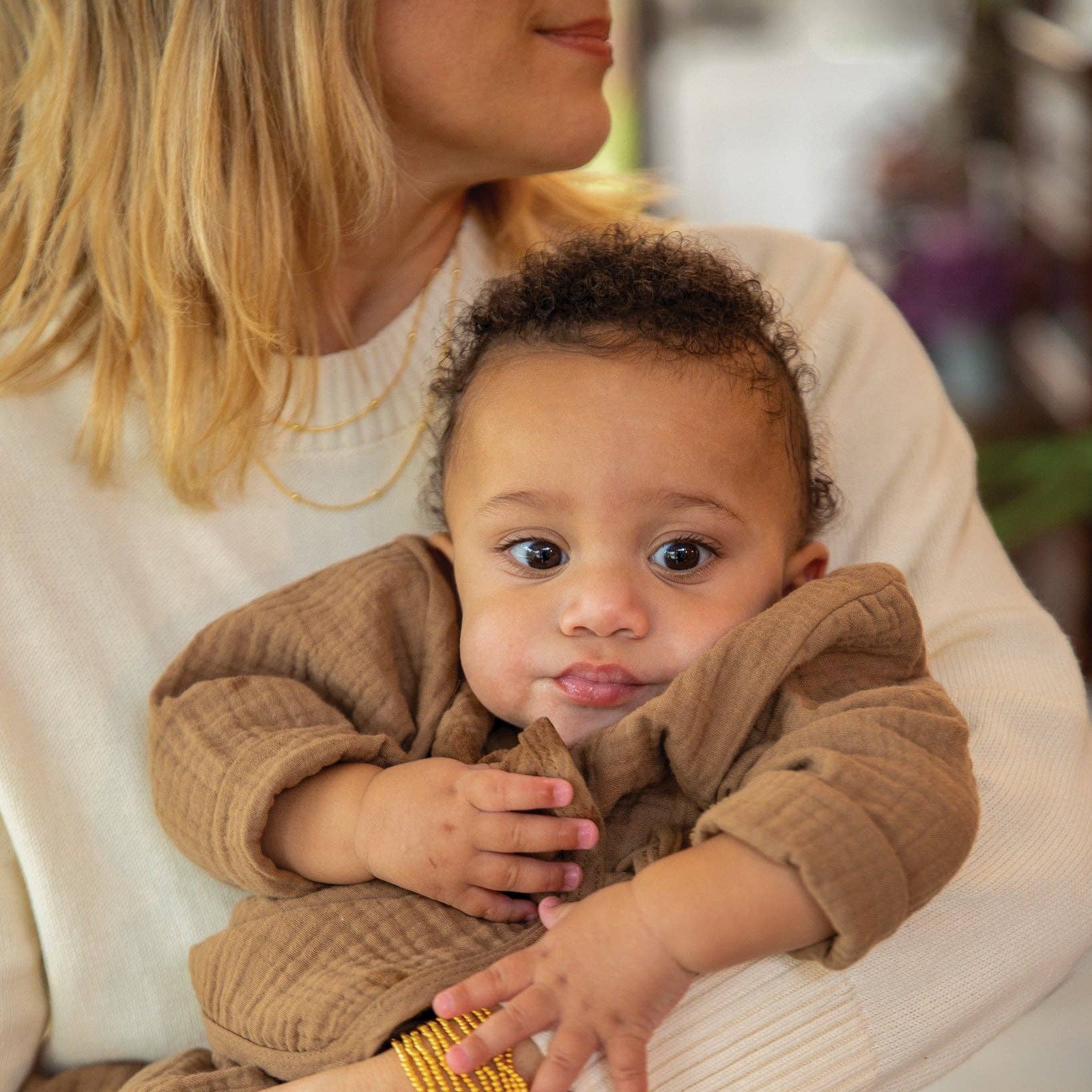 Baby in a brown outfit being held by a person with a blurred background