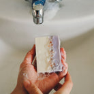 Hand holding a bar of soap under running water from a faucet.