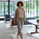 Woman in a gray outfit standing in a modern living room with large windows.