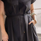 Person wearing a black dress with a belt, standing indoors.