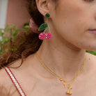 Close-up of a woman wearing colorful earrings and a gold necklace with a cherry pendant.