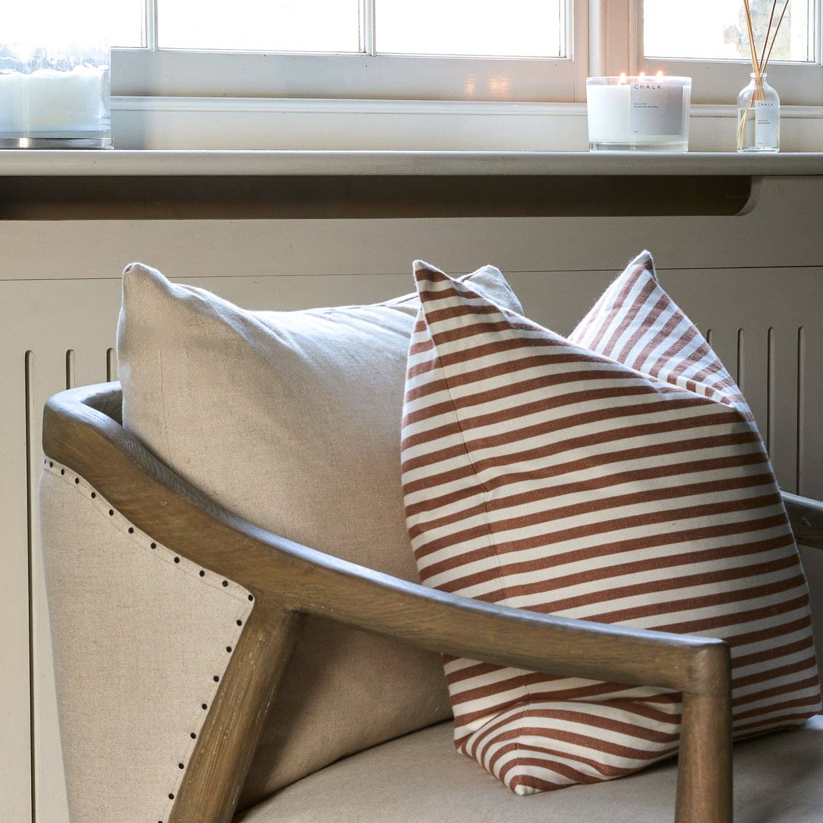 Decorative pillows on a wooden chair with a window and candles in the background