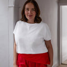 Woman wearing a white top and red pants standing indoors.