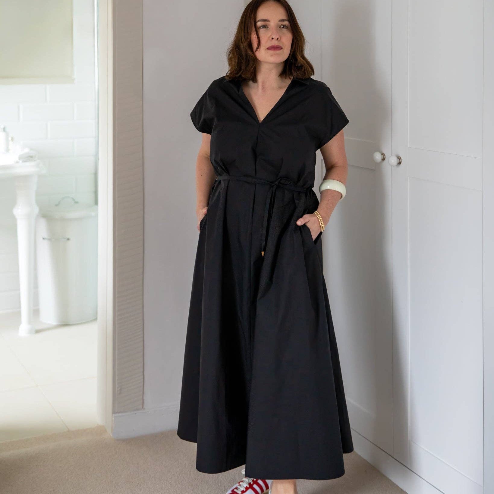 Woman wearing a black dress with white sneakers in a room.