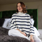 Woman wearing a striped sweater sitting on a bed with a green headboard.