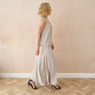 Woman wearing a beige skirt & blouse standing against a plain wall.