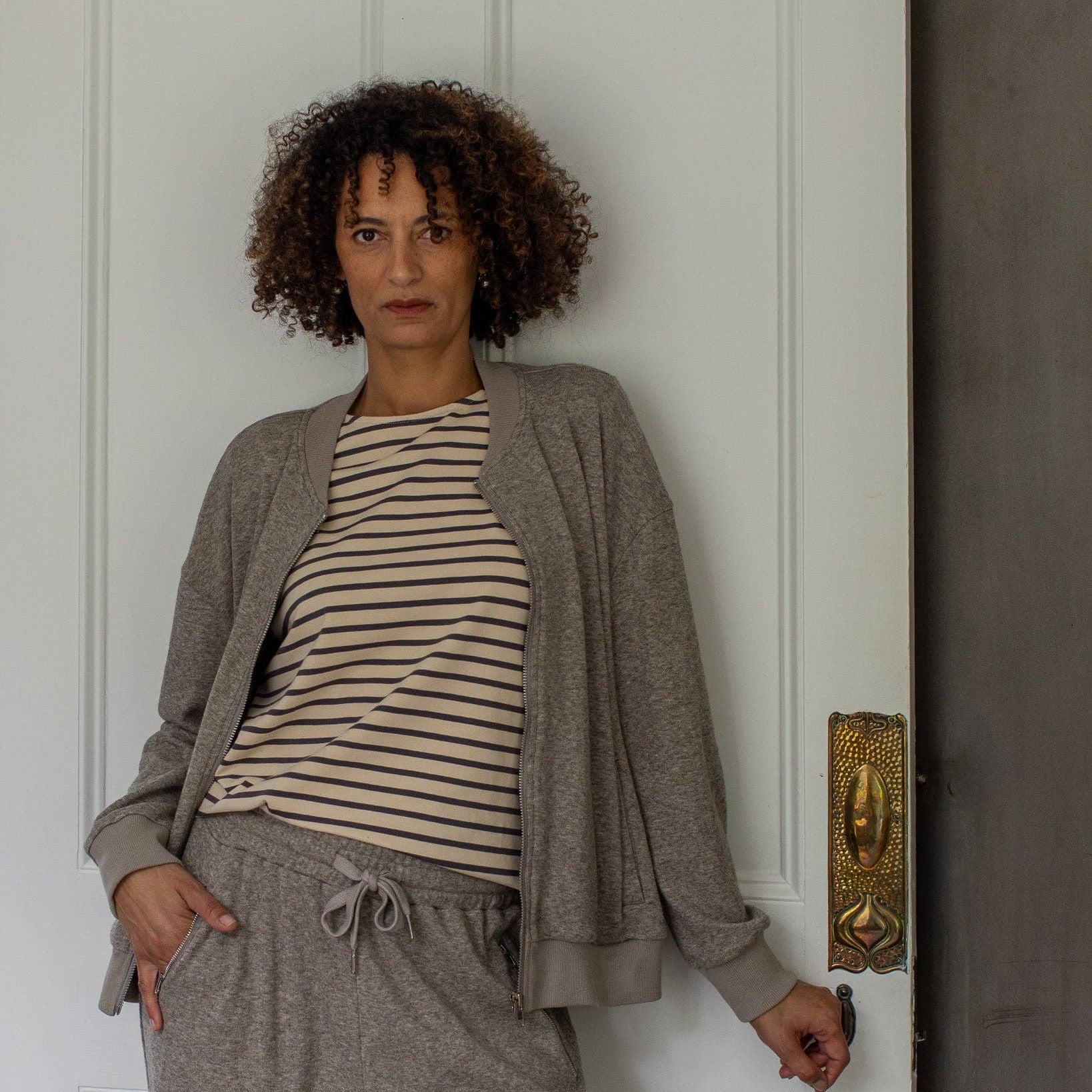 Woman wearing a striped shirt and gray cardigan standing in front of a white door.
