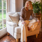Woman sitting on a white armchair in a room with large windows and plants.