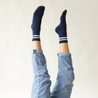 Person wearing navy socks with white stripes and light blue jeans against a plain background