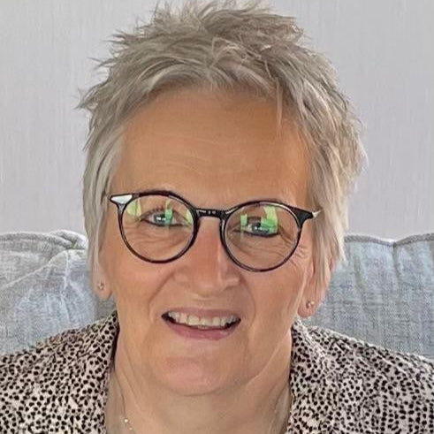 Person with short grey hair and glasses wearing a patterned shirt against a neutral background