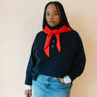 Person wearing a navy sweater with a red scarf and blue jeans against a beige background