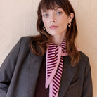 Woman wearing a gray coat and pink striped scarf against a beige background