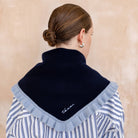 Person wearing a black scarf with ruffled edges over a striped shirt on a beige background