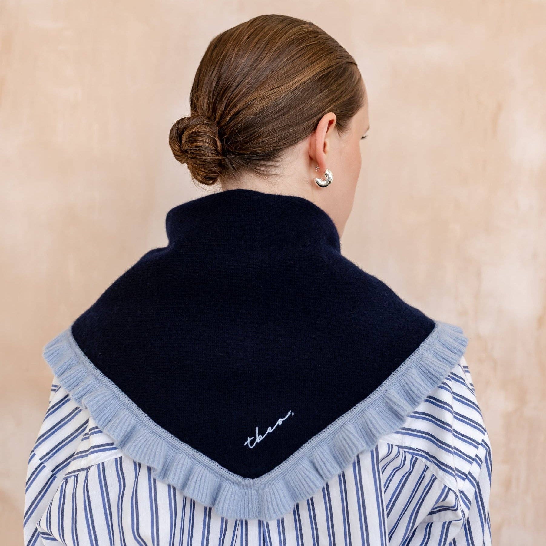 Person wearing a black scarf with ruffled edges over a striped shirt on a beige background