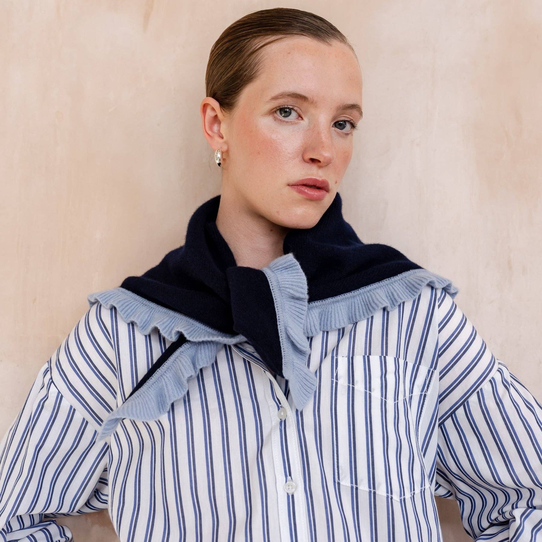 Person wearing a blue and white striped shirt with a black collar against a beige background