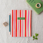 Striped notebook with a pencil, sharpener, and tape on a textured surface