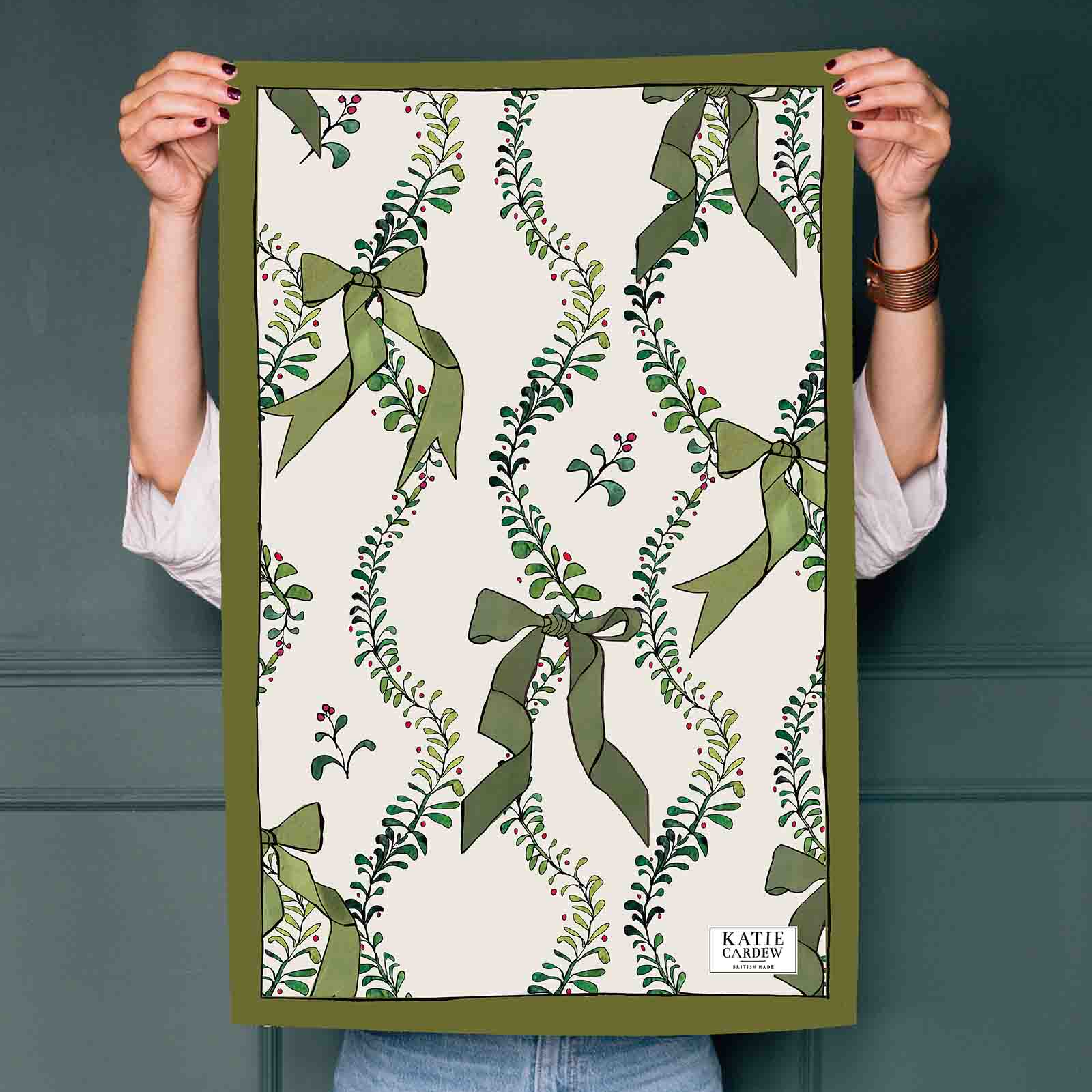 Person holding a tea towel with green leaf pattern against a dark wall