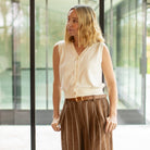 Woman wearing a white blouse and brown striped pants standing in a modern indoor setting.