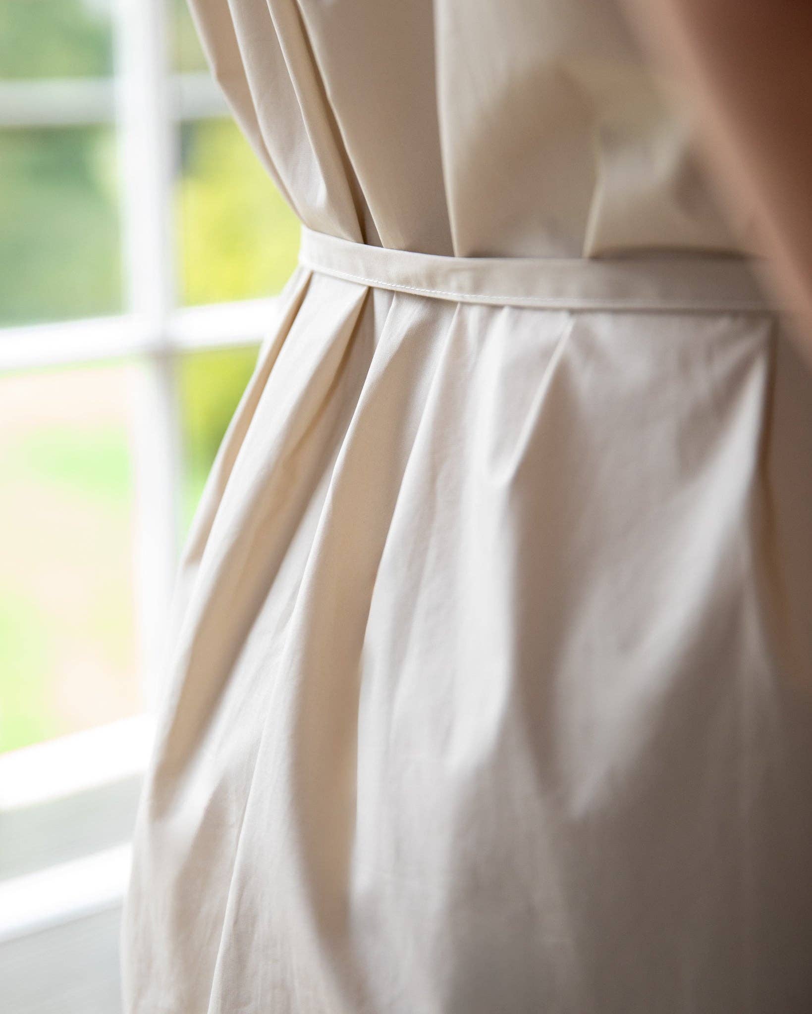 Close-up of a beige dress with a belt in front of a window