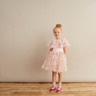 Young girl in a floral dress standing against a plain background