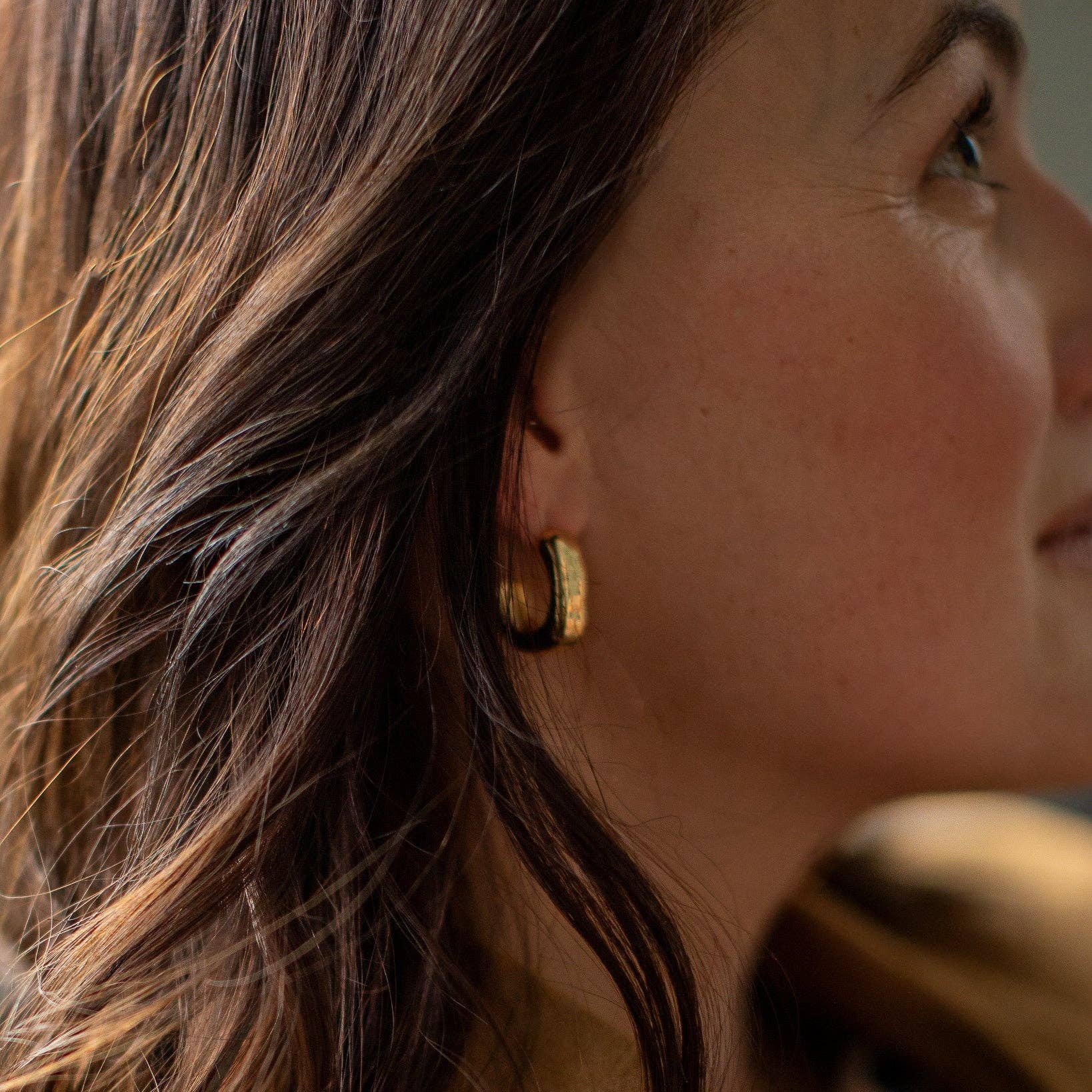 Close-up of a woman wearing gold hoop earrings with a blurred background