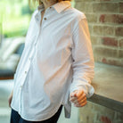 Person wearing a white button-up shirt with a pink collar against a brick wall.