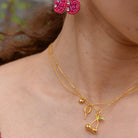Close-up of a person wearing gold earrings and necklace with cherry design.
