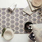 A table setting with a slate blue floral patterned fabric from Olive & Daisy, with a white bowl, wooden vase, and greenery decor.